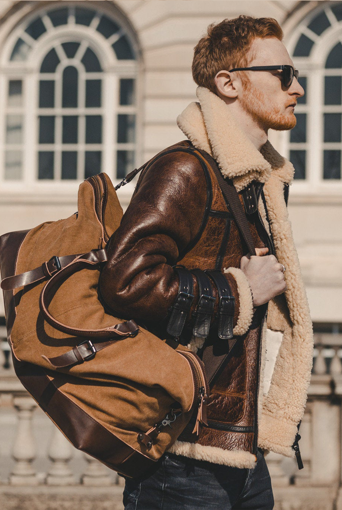 Man_wearing_a_brown_leather_jacket_with_fur_lining_holding_a_matching_backpack_in_front_of_a_building.-1