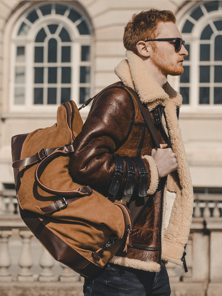 Man_wearing_a_brown_leather_jacket_with_fur_lining_holding_a_matching_backpack_in_front_of_a_building.-1