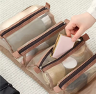 Clear travel organizer with zippers being held open by a hand, on a light background.